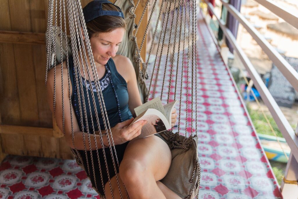 A woman enjoying 100 Hour Yoga Teacher Training in Goa, sitting in a hammock and reading a book.