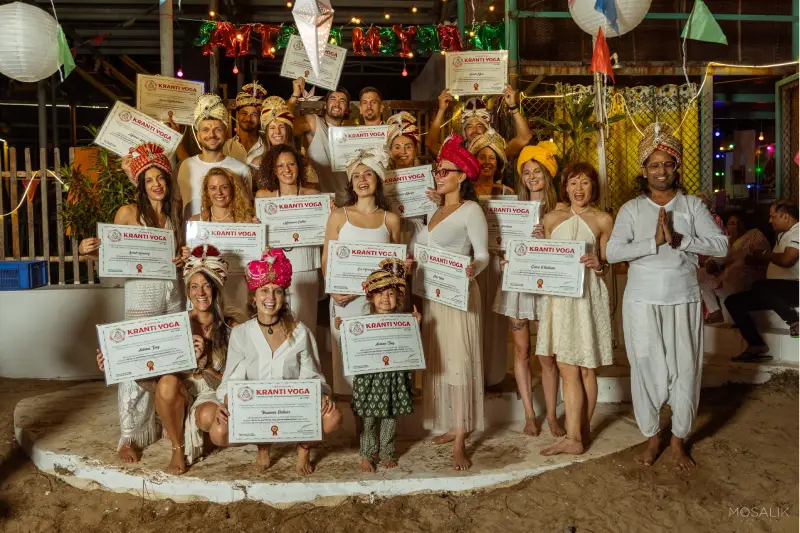 A group of people holding certificates from their 200 Hour Yin & Vinyasa TTC on the beach.