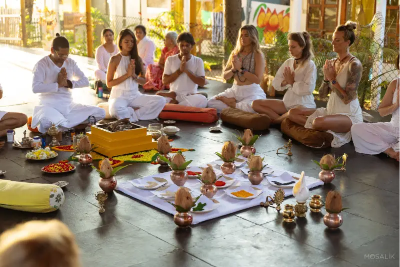 A group of people in white robes participating in a 200 Hr Hatha & Vinyasa TTC, sitting around a table.