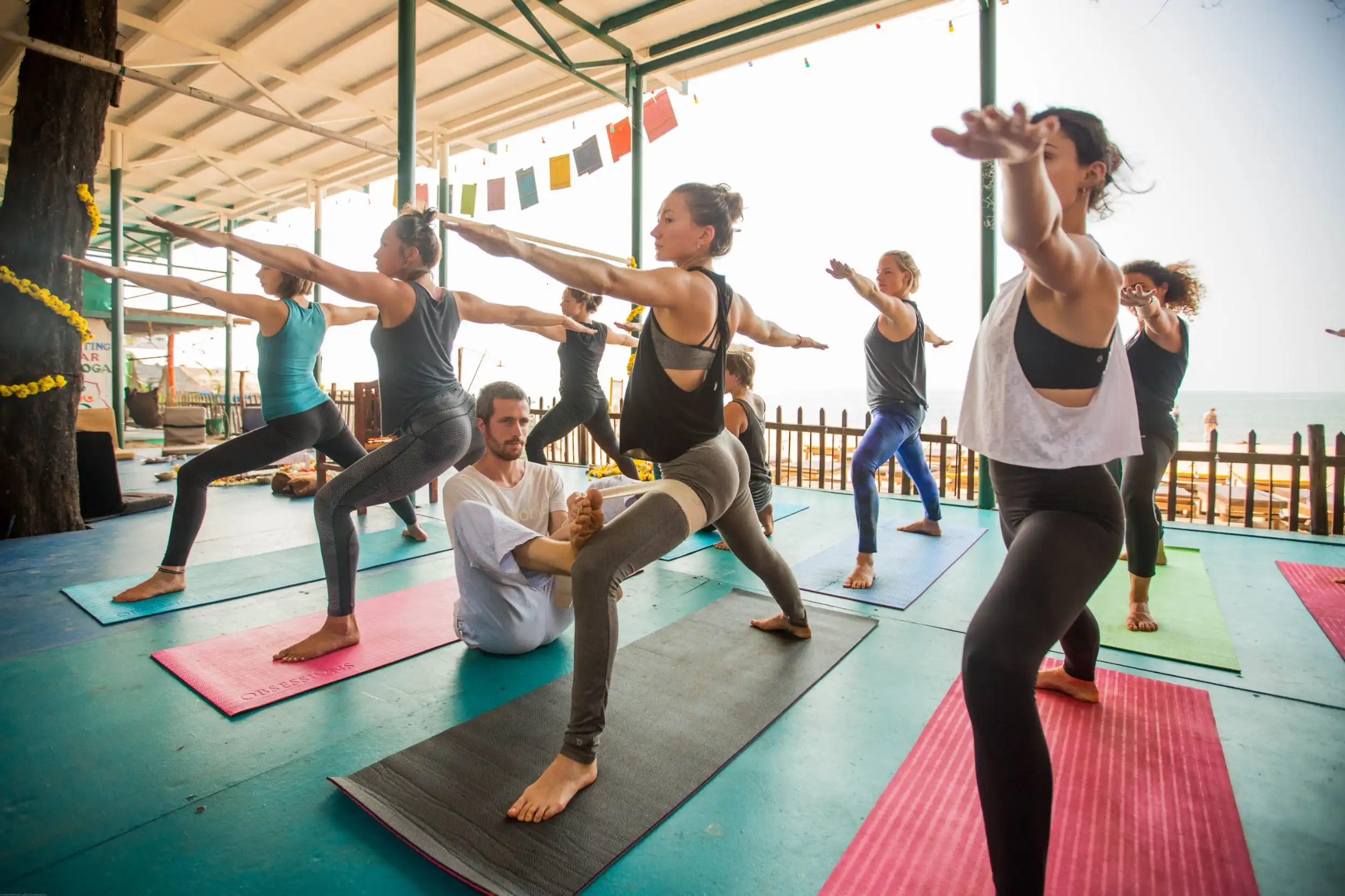 Group of people practicing yoga outdoors in a large area, Yoga TTC Goa.