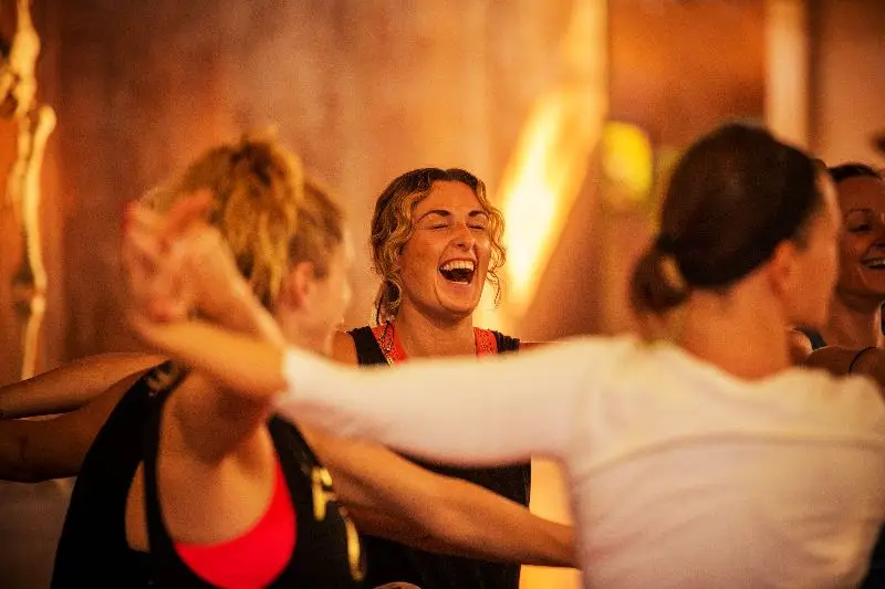 A lively group of women joyfully dancing and laughing in a room during a 50 hr yoga in Goa.