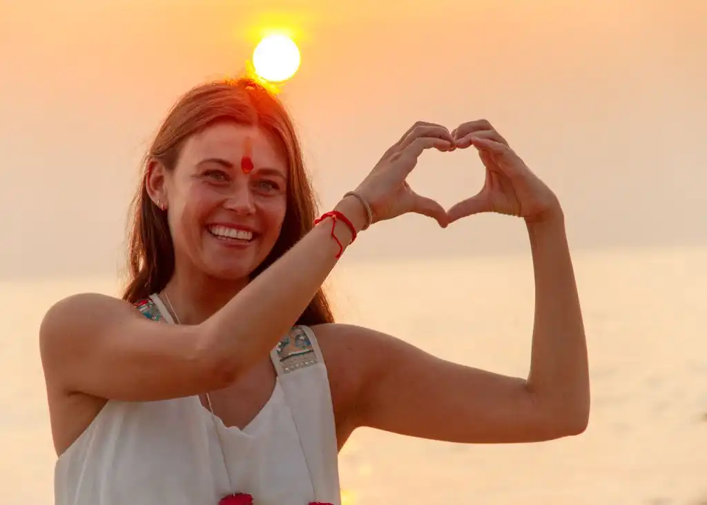 Woman forming heart shape with hands on beach, 100 yoga tcc in Goa, India.